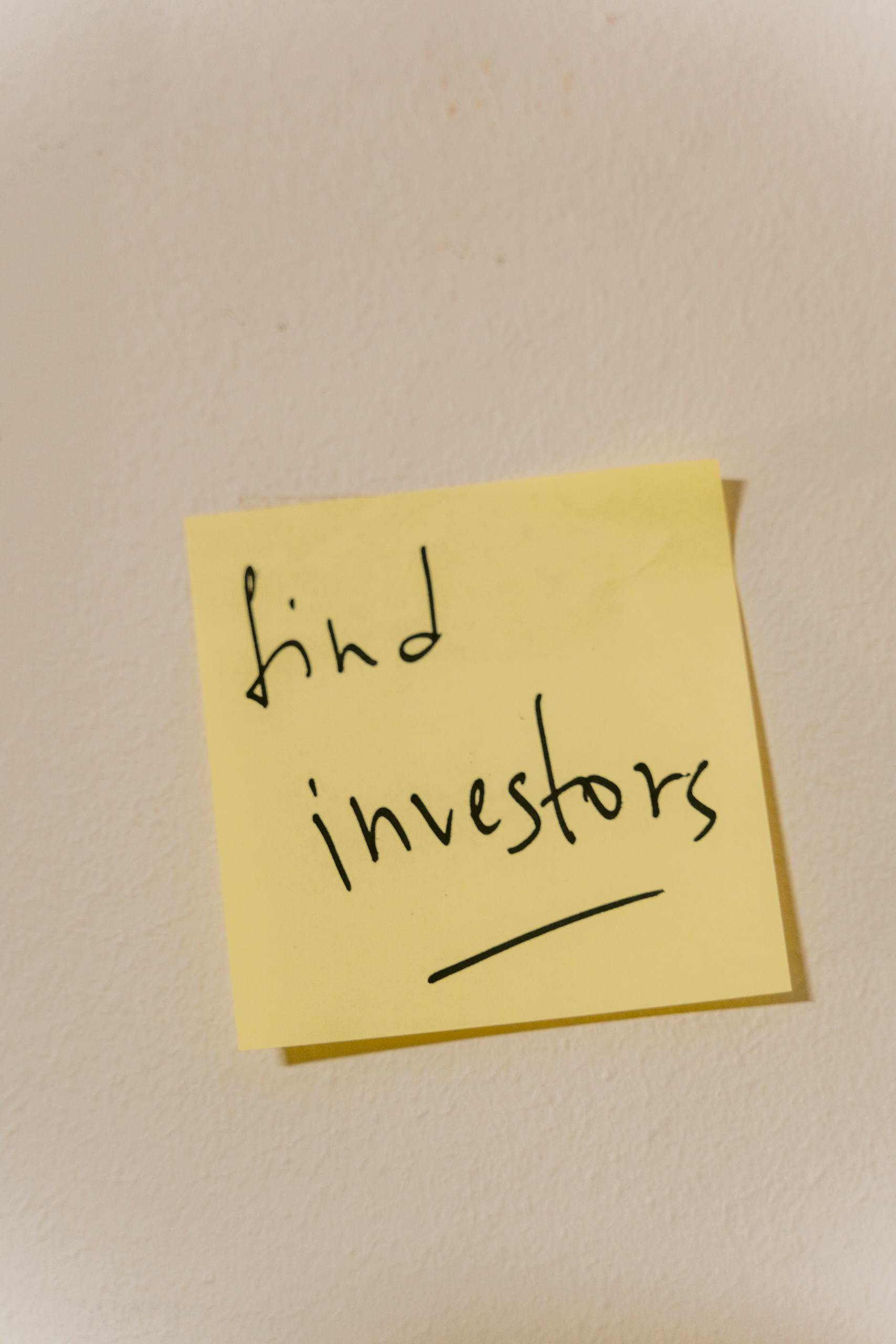 Close-up of a handwritten note reminding to find investors, on a wall.
